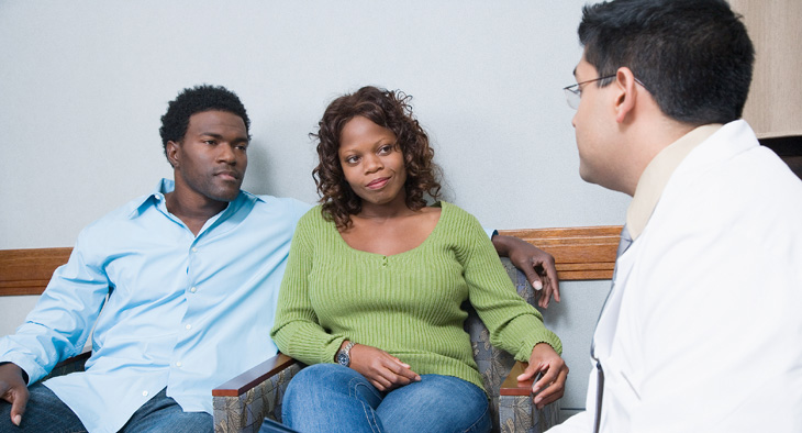 A photo of a man and woman, a couple, listening to a doctor during a medical consultation.