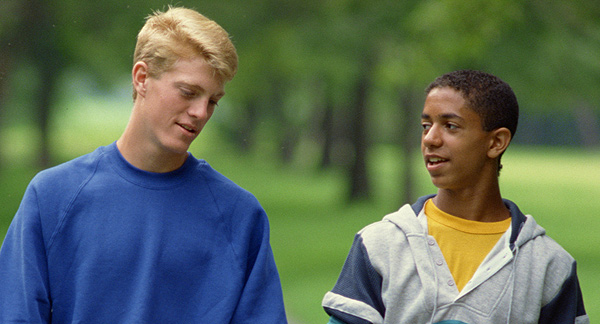 A photo of two young men walking and talking in a park or forest. 