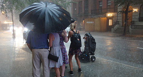 A photo of a family under an umbrella in the street in heavy rain.