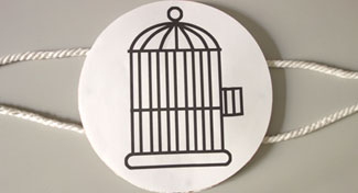A photo of a moving image toy. A birdcage is drawn on one side of a square piece of card. There are strings on each side of the card. 