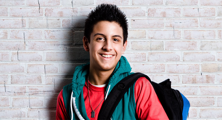 A photo of a boy in a jacket with as bag on his back. He is a teenager.