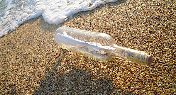 A photo of a bottle washed up on a beach. Inside the bottle there is a rolled up piece of paper or a document of some kind. 