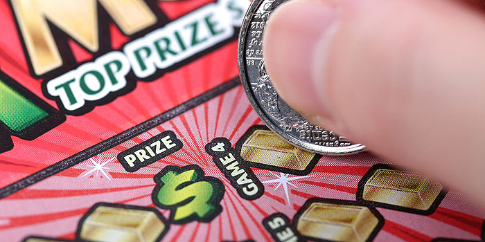 A photo of a hand holding a coin, scratching the coin on a lottery scratch card. 