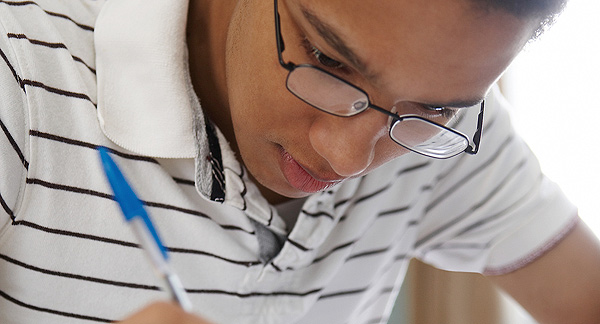 A photo of a teenager concentrating and writing with a pen. 