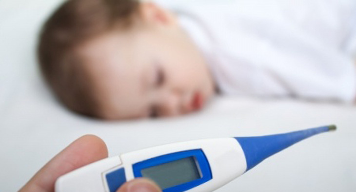 A photo of young child ill in bed and a hand holding a thermometer.