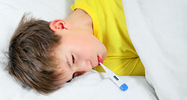 A photo of an ill child in a bed with a thermometer in his mouth.