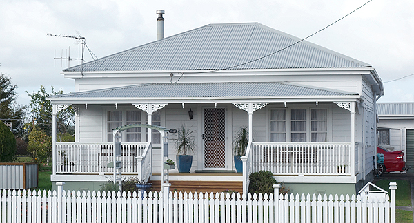 A photo of suburban house with a garden and white front fence.