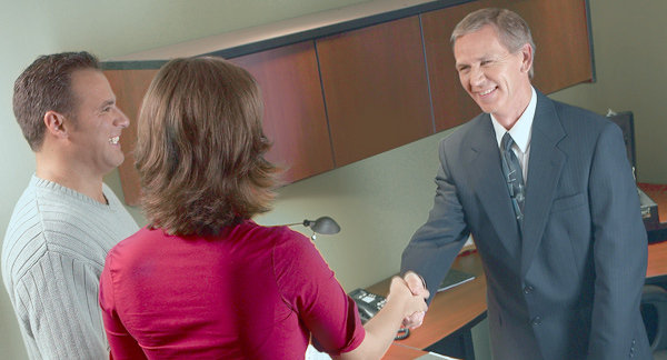 A photo of a bank manager shaking hands with a woman and her partner.