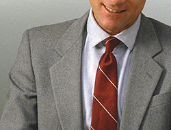 A photo of a man in a grey jacket and red tie.
